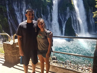 picture of a man and woman smiling next to a waterfall