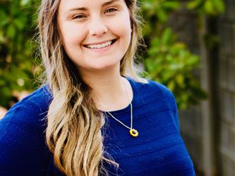 picture of a woman with brown hair, blue shirt, and a necklace on smiling